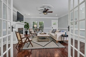 A spacious living room with a fireplace, wooden flooring, and a ceiling fan.