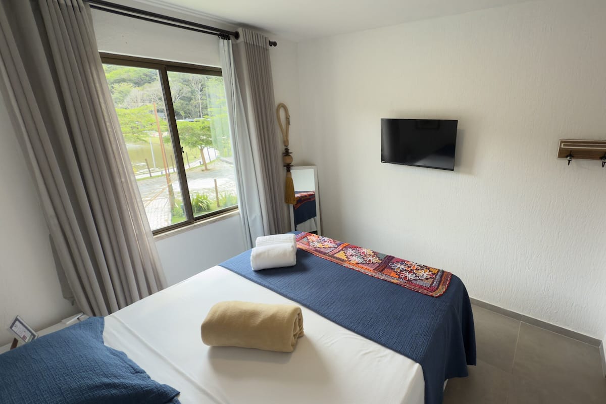 A hotel room with a bed, a TV on the wall, and a window with curtains.