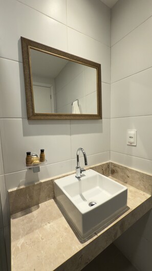 Un baño con lavamanos blanco, un espejo y artículos de tocador sobre la encimera.
