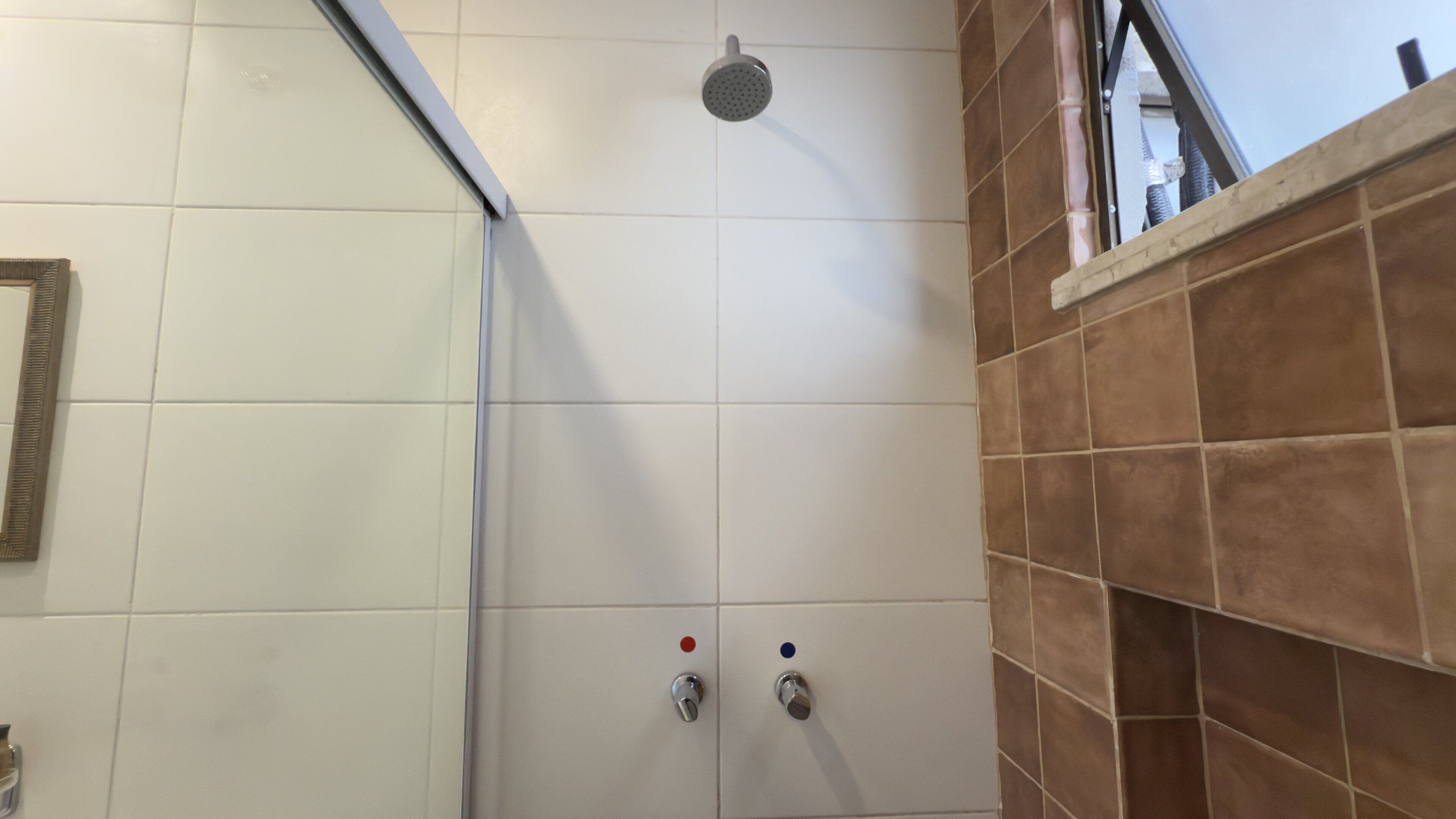 Une douche équipée d’un pommeau de douche à main, d’un panneau de commande avec des boutons rouges et bleus, et d’un mur carrelé.