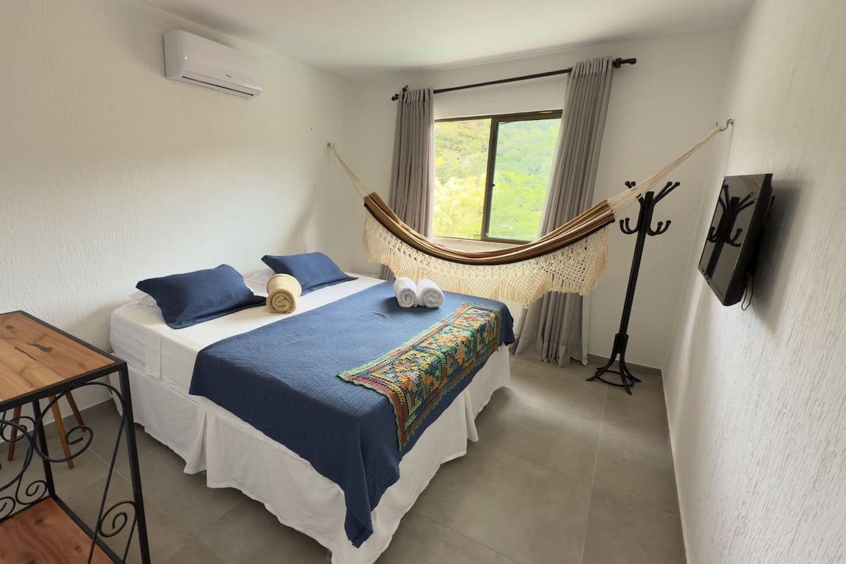 A bedroom with a bed, a hammock, a TV, and a small table.