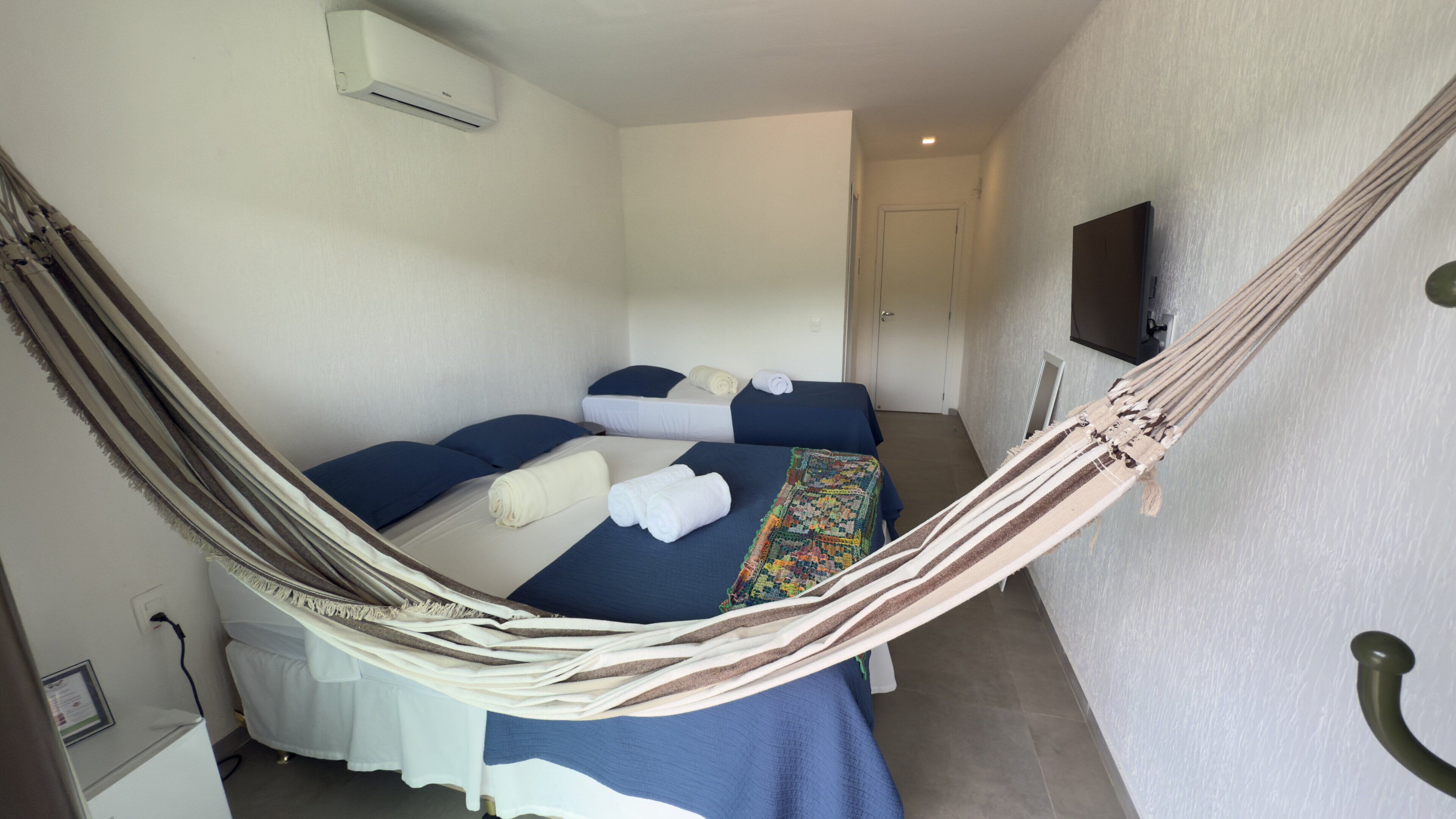 Una habitación con dos camas, una hamaca, un televisor y una puerta.