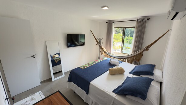 Un dormitorio con una cama, una hamaca, un televisor y una ventana con cortinas.