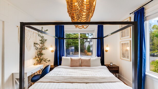 Quarto com cama grande, escrivaninha, cadeira, planta e vista exterior.