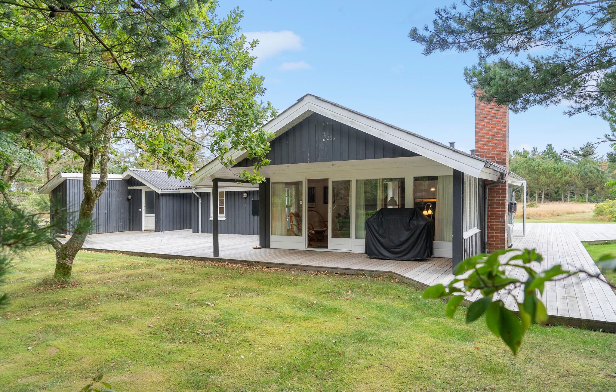 Une maison moderne dotée d’un patio couvert, d’une cheminée en briques et d’une grande porte-fenêtre coulissante.