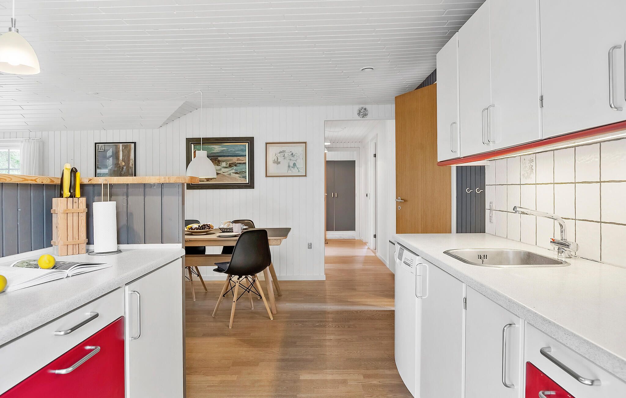 A modern kitchen with white cabinets, a wooden dining table, and a red chair.