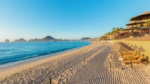 Ein Strand mit einer Reihe von Liegestühlen und Sonnenschirmen, einem klaren, blauen Himmel und ruhiger See.