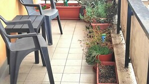 A balcony with plastic chairs, potted plants, and a railing.
