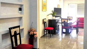 A modern living room with a dining area, featuring a red chair, a vase with flowers, and a painting on the wall.