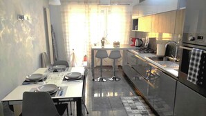 A modern kitchen with a dining area, stainless steel appliances, and a window with curtains.