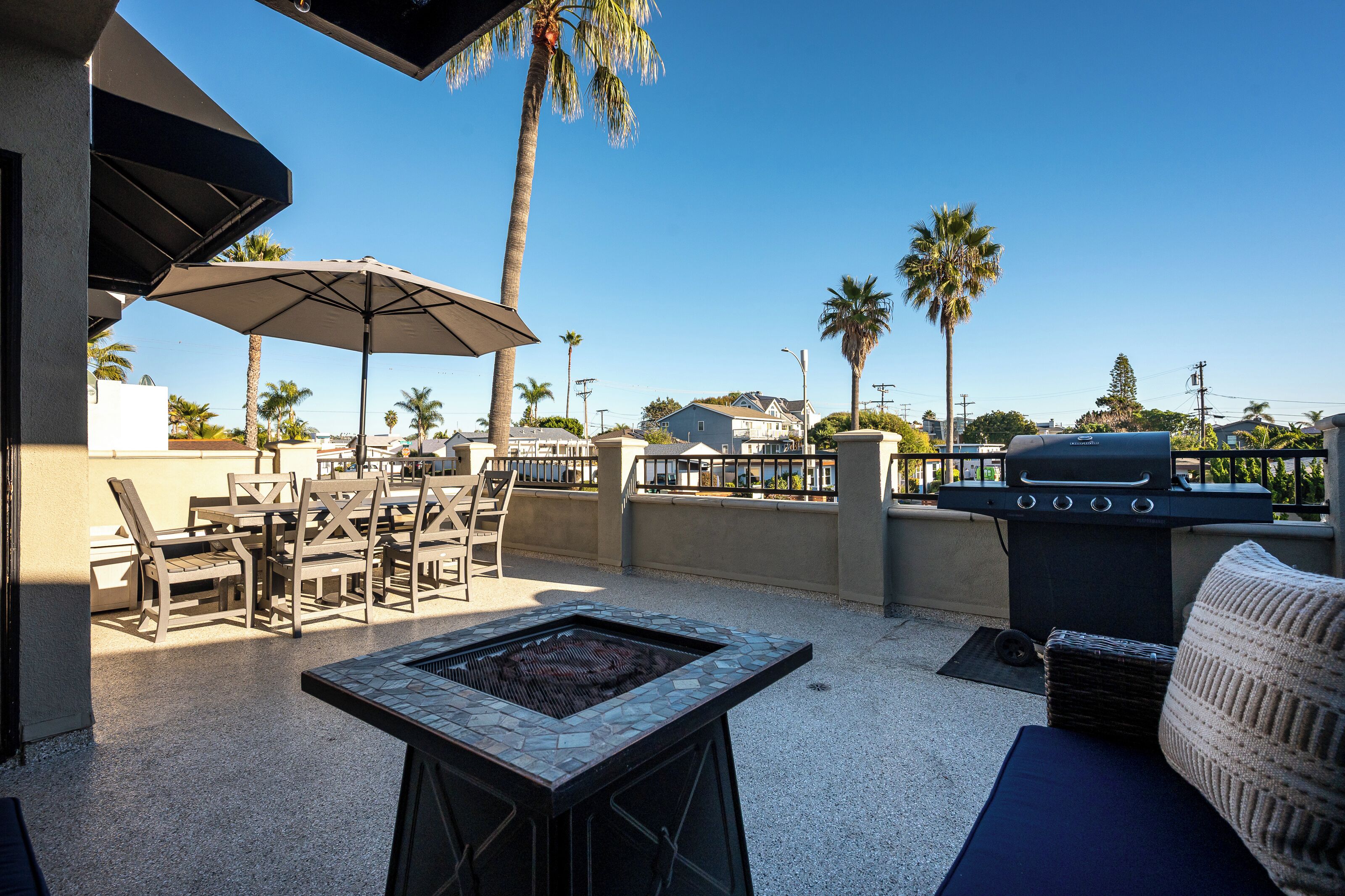 An outdoor patio with a grill, seating area, and umbrellas.