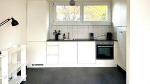 A modern kitchen with white cabinets, a black countertop, a window with a view of trees, a black pendant light, and a built-in oven.
