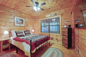 A wooden cabin bedroom with a bed, nightstands, a dresser, a ceiling fan, and a window with blinds. - Dog-Friendly Creek Cabin | Trail Access, Hot Tub & Fire Pit (Blue Ridge)