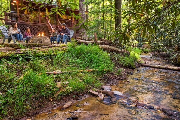 A natural setting with a wooden deck, a fire pit, and a stream.