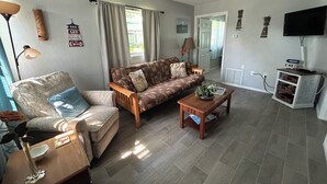 Ein Wohnzimmer mit einer Couch, einem Sessel, einem Couchtisch und einem Fernseher.
