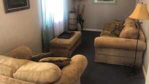 A living room with two beige sofas, a coffee table, a TV mounted on the wall, and a lamp.