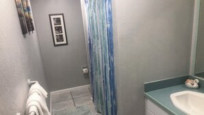 A bathroom with a white sink, a towel rack with a white towel, a framed picture on the wall, and a blue shower curtain.