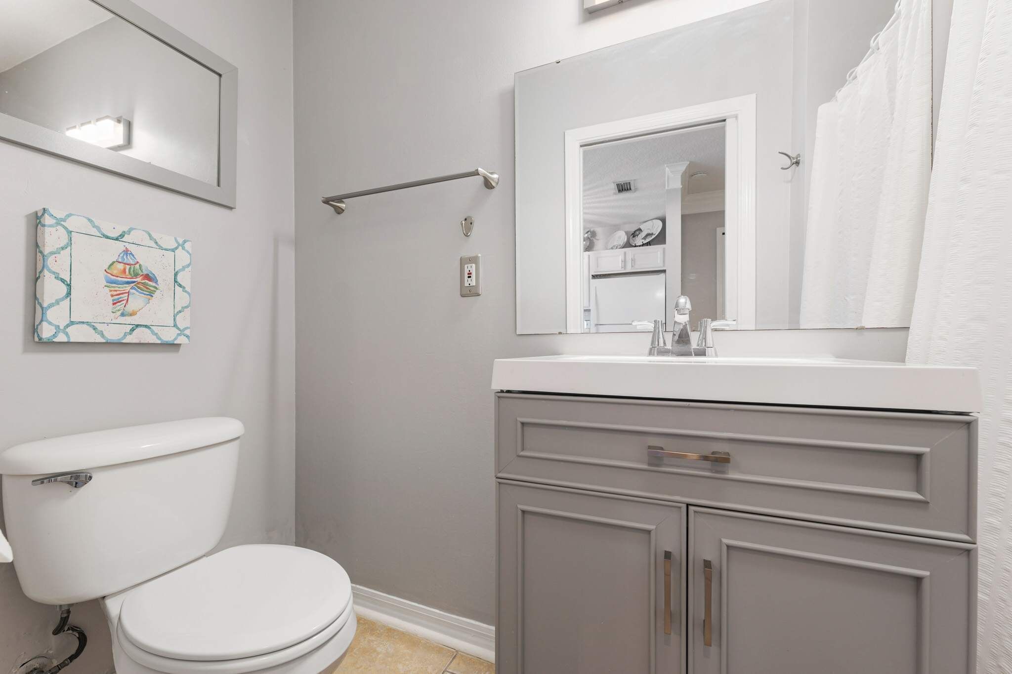 A bathroom with a white toilet, grey cabinets, a white sink, and a mirror above the sink.
