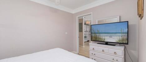 A bedroom with a bed, a dresser, a television displaying a beach scene, and a ceiling fan.