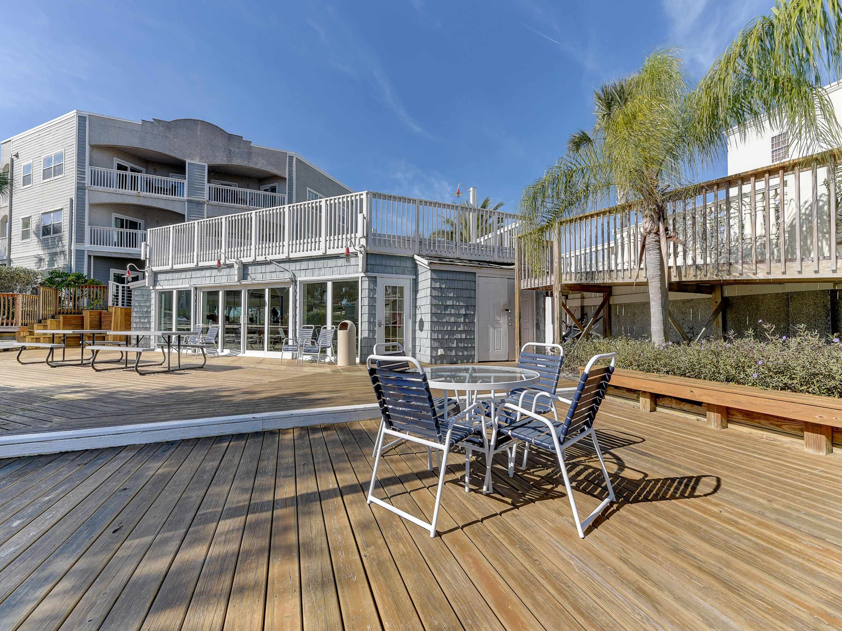 A wooden deck with outdoor seating, a building with a balcony, and a palm tree.