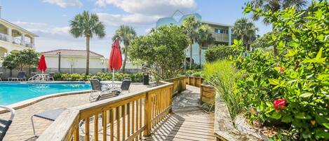 A wooden deck with a pool, lounge chairs, and a red umbrella.