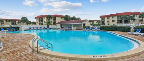 A swimming pool with blue water, surrounded by lounge chairs and a brick deck.