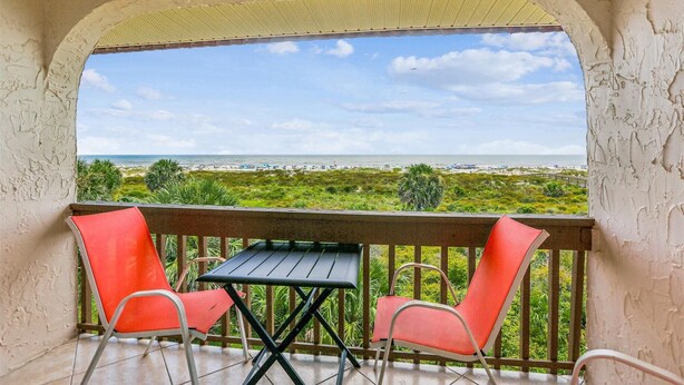 A balcony with two red chairs and a table, overlooking a beach with a clear sky. - Serene St. Augustine Ocean & Racquet 8315 Getaway (St. Augustine)