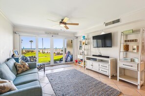 A living room with a sofa, a television, a bookshelf, and a view of the beach through the sliding glass door. - Oceanic Luxury: Historic St. Augustine Gem (St. Augustine)
