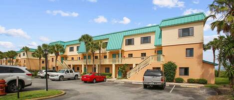 A multi-story hotel with a green roof, a parking lot, and palm trees.