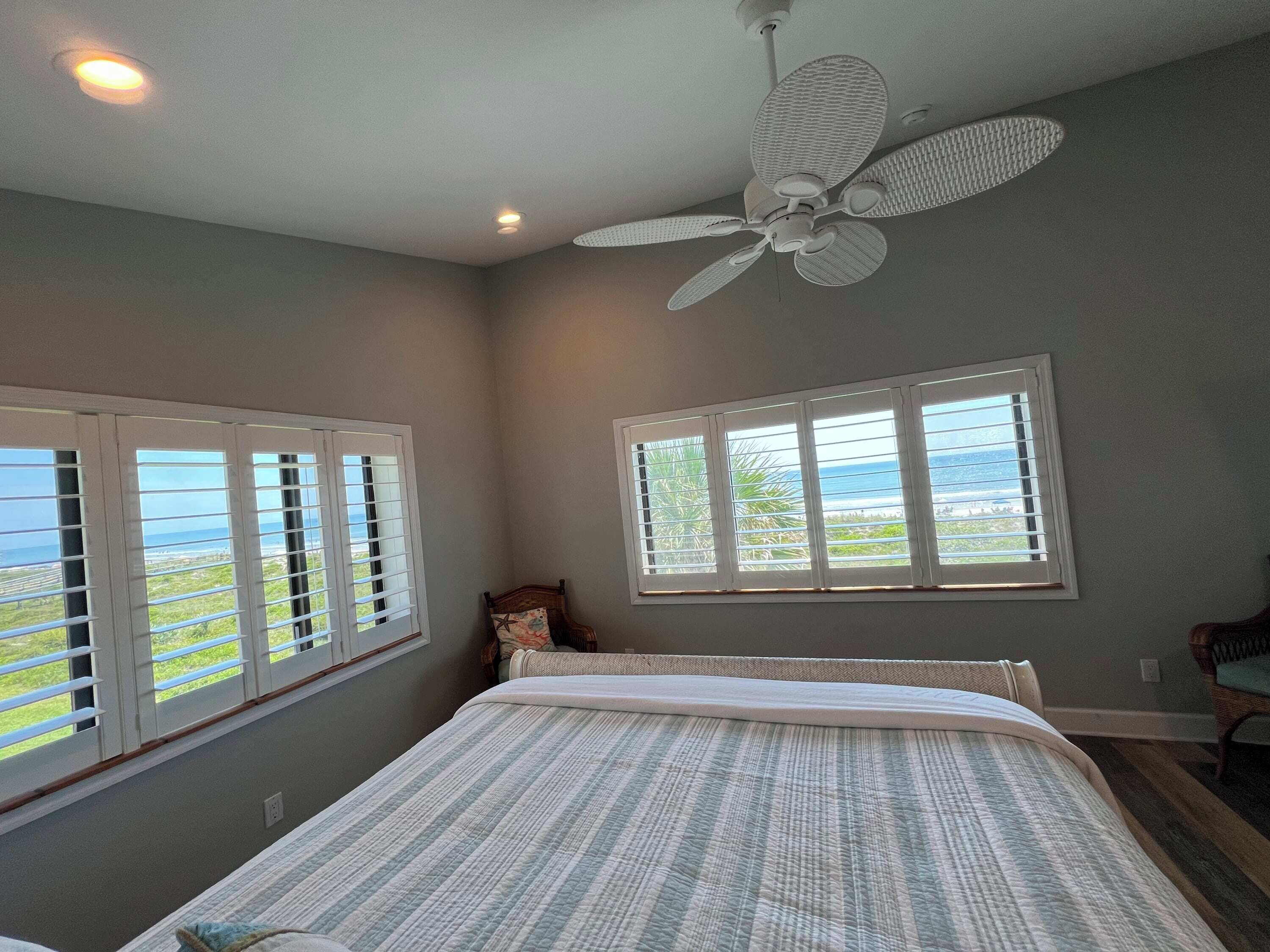 A bedroom with a bed, a ceiling fan, and two windows with blinds.