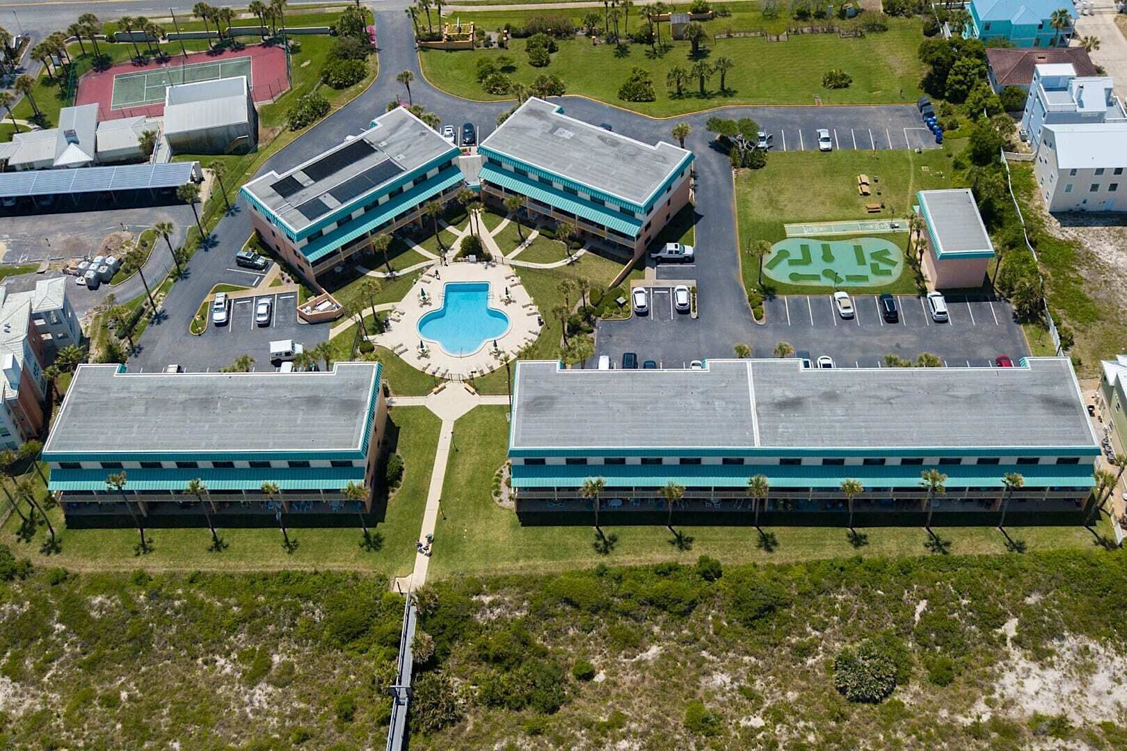 An aerial view of a campus with three main buildings, a central courtyard with a swimming pool, and a parking area.