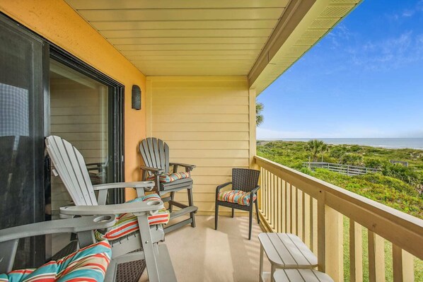 A balcony with two Adirondack chairs and a small table, overlooking a coastal landscape. - St. Augustine's Luxury Beachfront Oasis (St. Augustine)