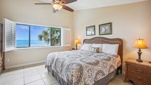 Ein Schlafzimmer mit einem großen Bett, einem Deckenventilator, einem Fenster mit Rollläden und Blick aufs Meer.