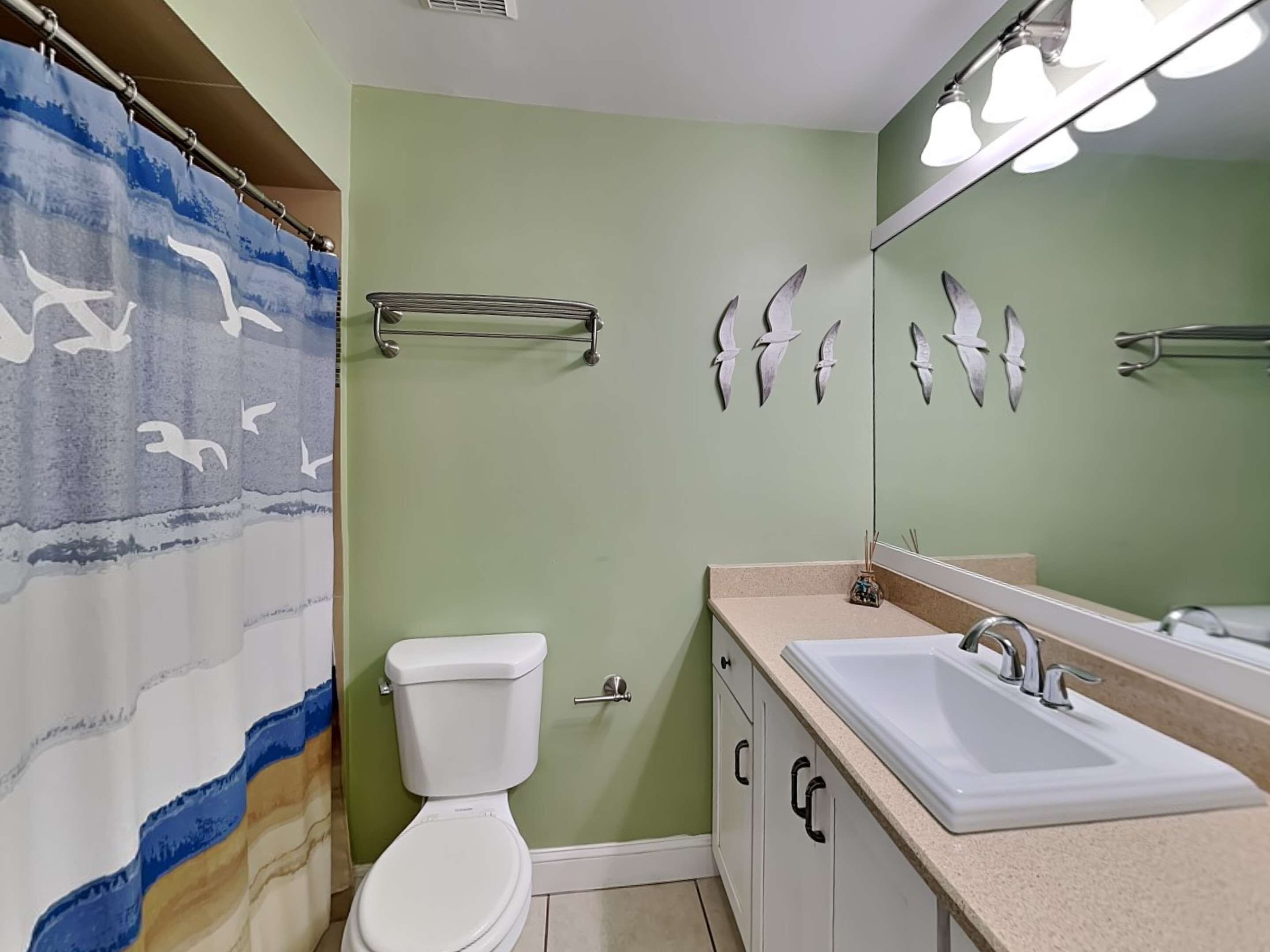 A bathroom with a shower curtain, toilet, sink, and mirror.