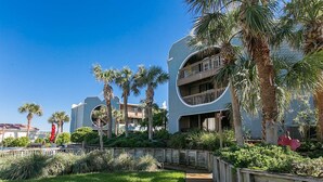 Un hotel moderno con una facciata curva, un pontile in legno e palme.