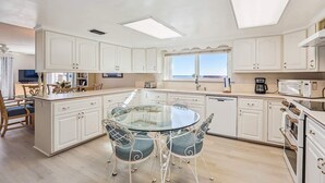 A modern kitchen with white cabinetry, a glass dining table, and a view to the outside. - Oceanfront 3BR Condo: Gated, Breathtaking View (St. Augustine)