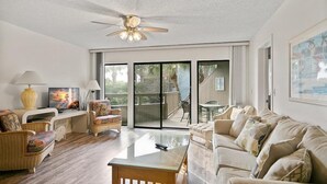 A spacious living room with a ceiling fan, large sliding glass doors leading to an outdoor area, and a variety of seating options including a sofa and chairs. - Unwind at St Augustine's Beachfront Oasis (St. Augustine)