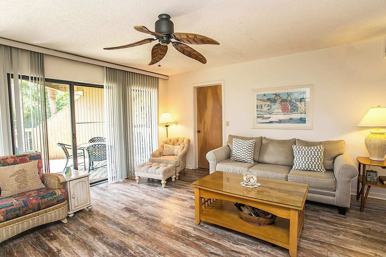 A living room with a sofa, armchair, ottoman, coffee table, and a ceiling fan.