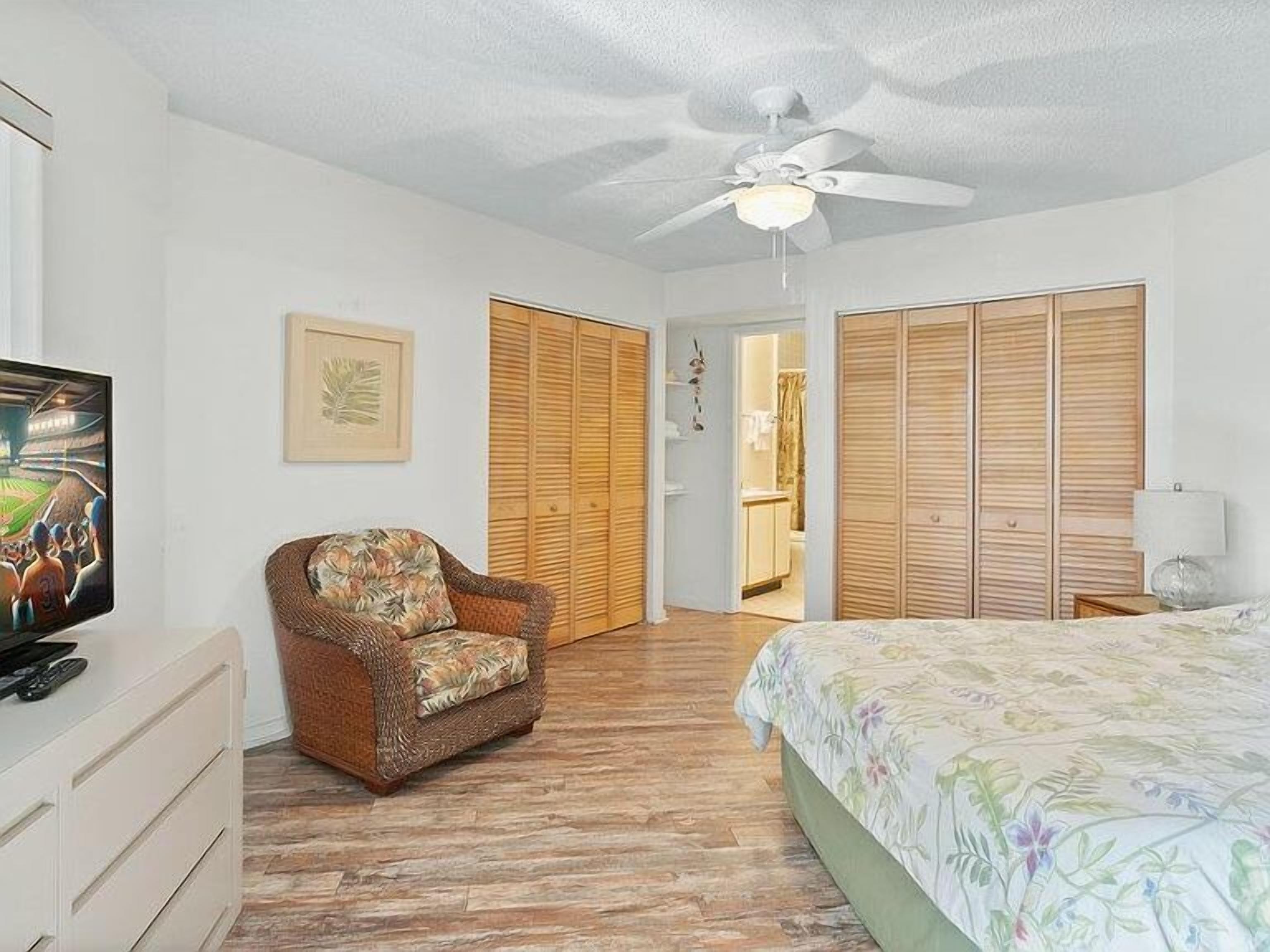A bedroom with a bed, a chair, a ceiling fan, a wardrobe, and a television.