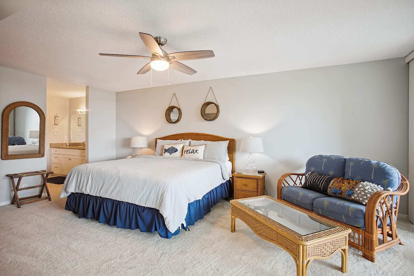 Une chambre à coucher comprenant un lit, des tables de chevet, une chaise, un ventilateur de plafond et un miroir.