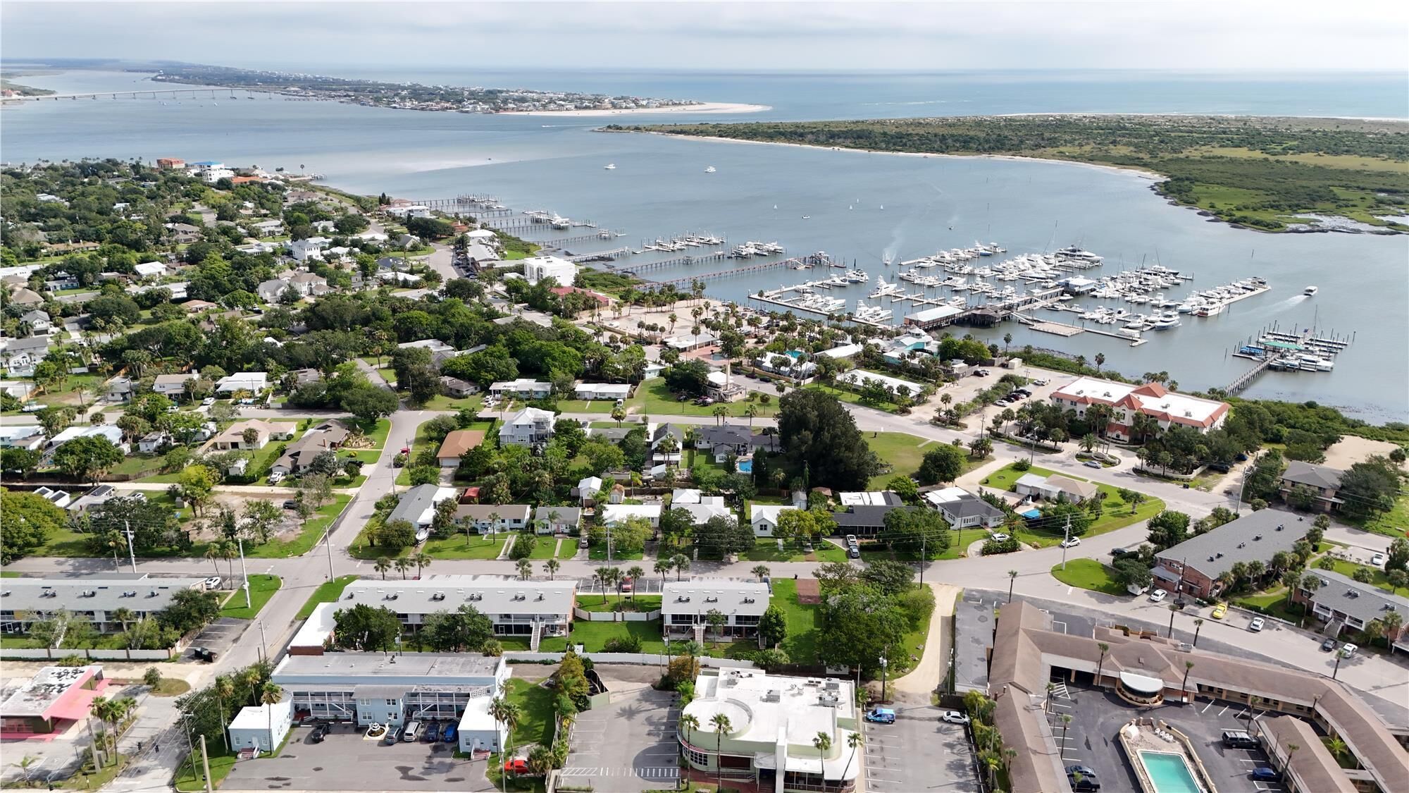 An aerial view of a coastal town with a marina, residential areas, and a large hotel with a swimming pool.