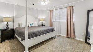A bedroom with a four-poster bed, a ceiling fan, and a window with curtains.