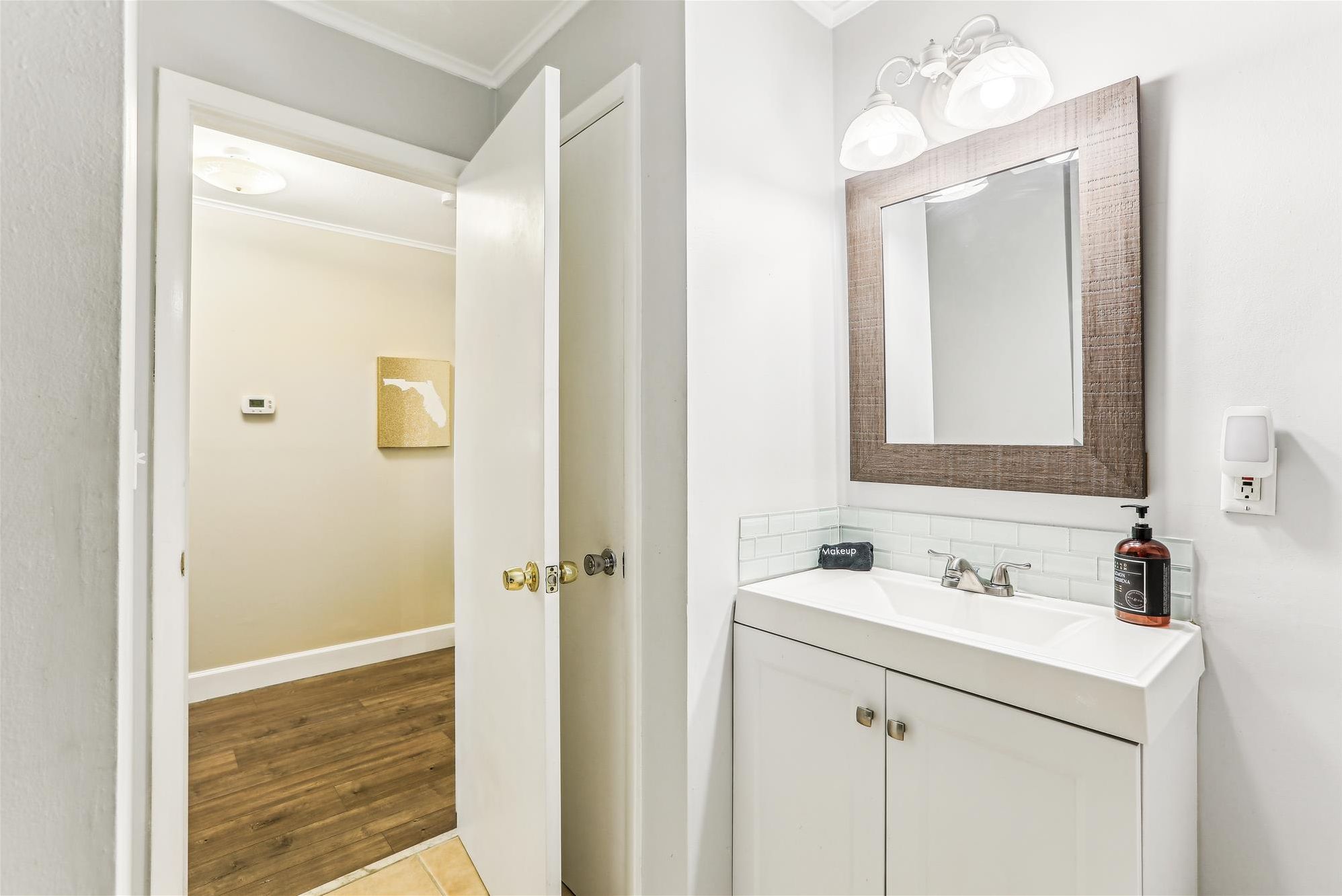 A bathroom with a white vanity, a mirror with a wooden frame, and a wall-mounted light fixture.
