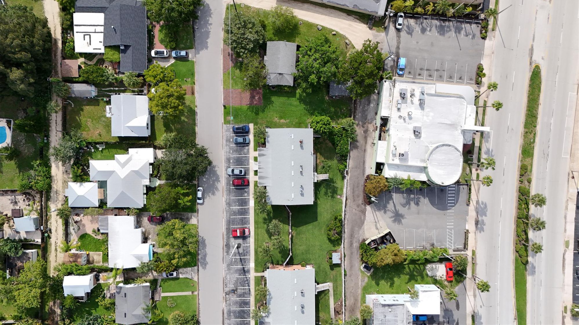 An aerial view of a residential area with houses, a parking lot, and a large building with a flat roof.