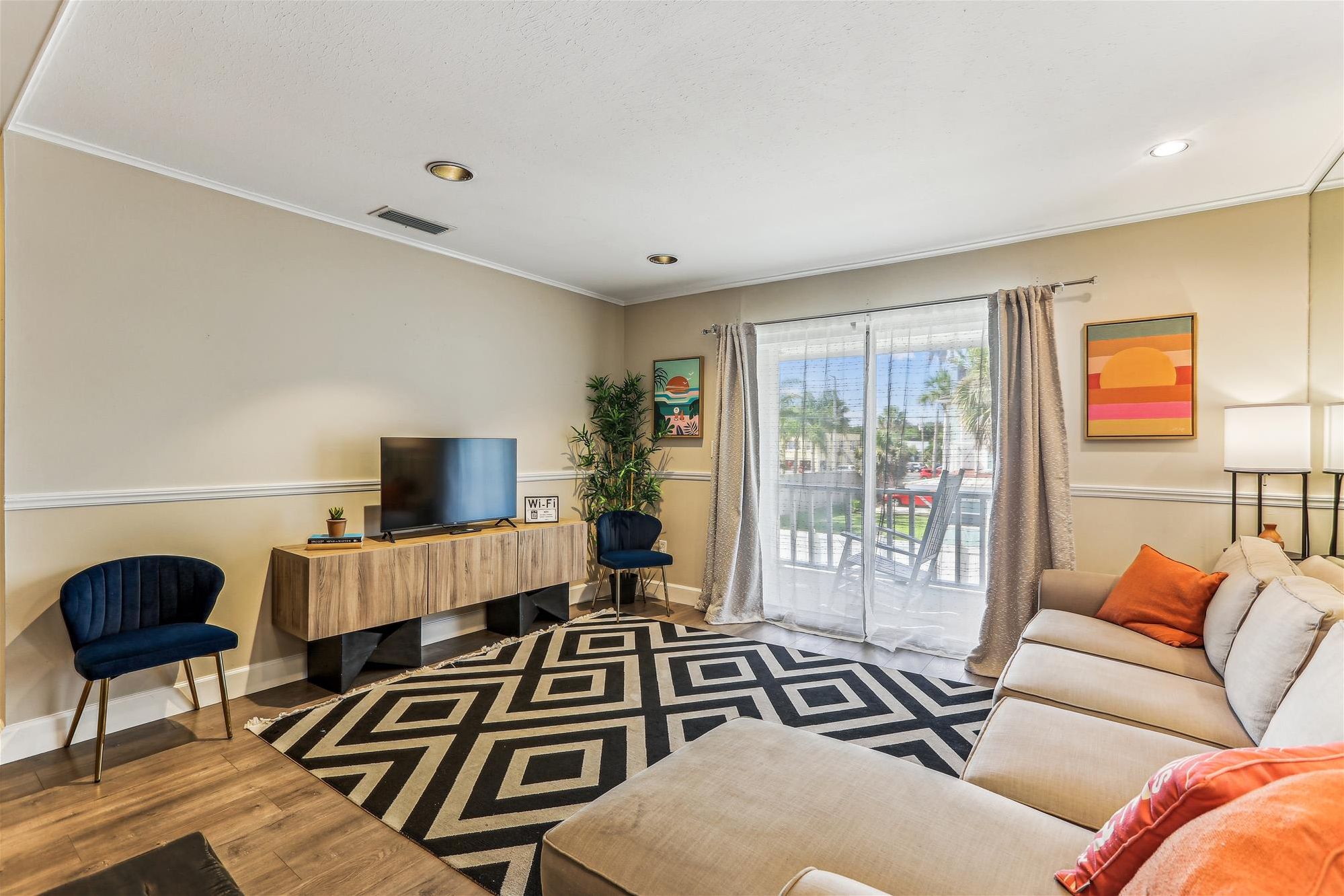 A living room with a TV, a sofa, a coffee table, a patterned rug, and a large window with curtains.
