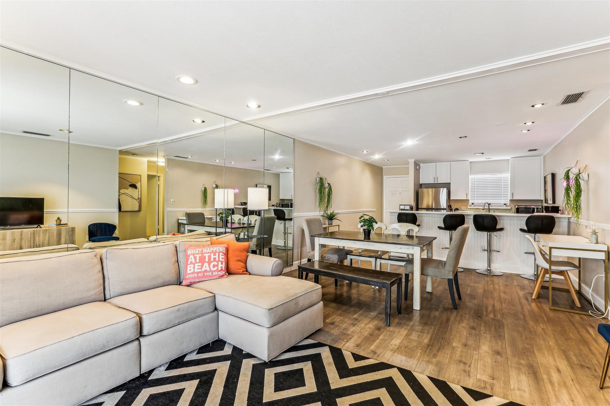A modern living room with a sectional sofa, a dining area with a wooden table, and a kitchen with white cabinets.