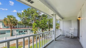 A covered porch with a white railing, a white rocking chair, and a door.