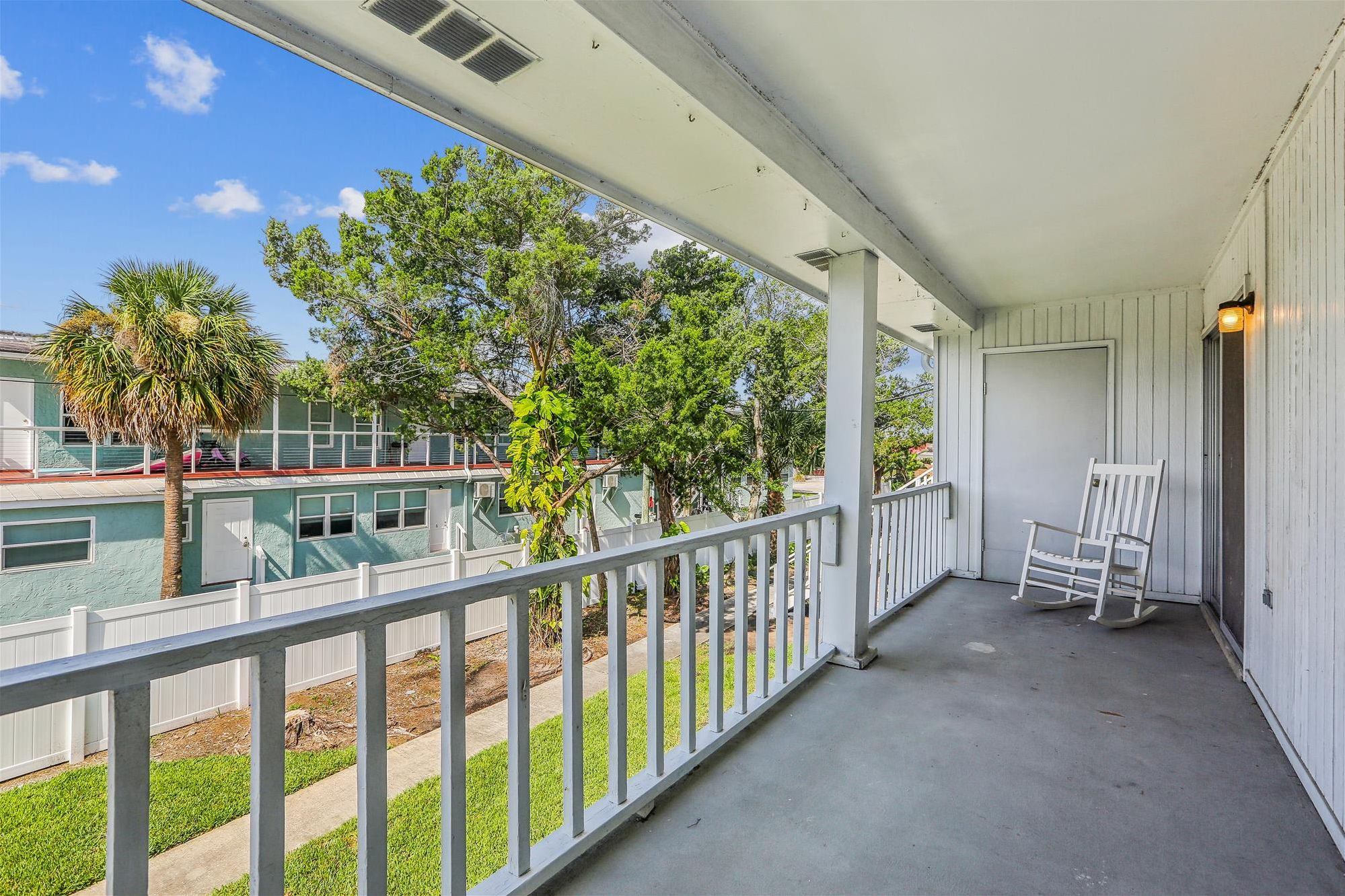A covered porch with a white railing, a white rocking chair, and a door.