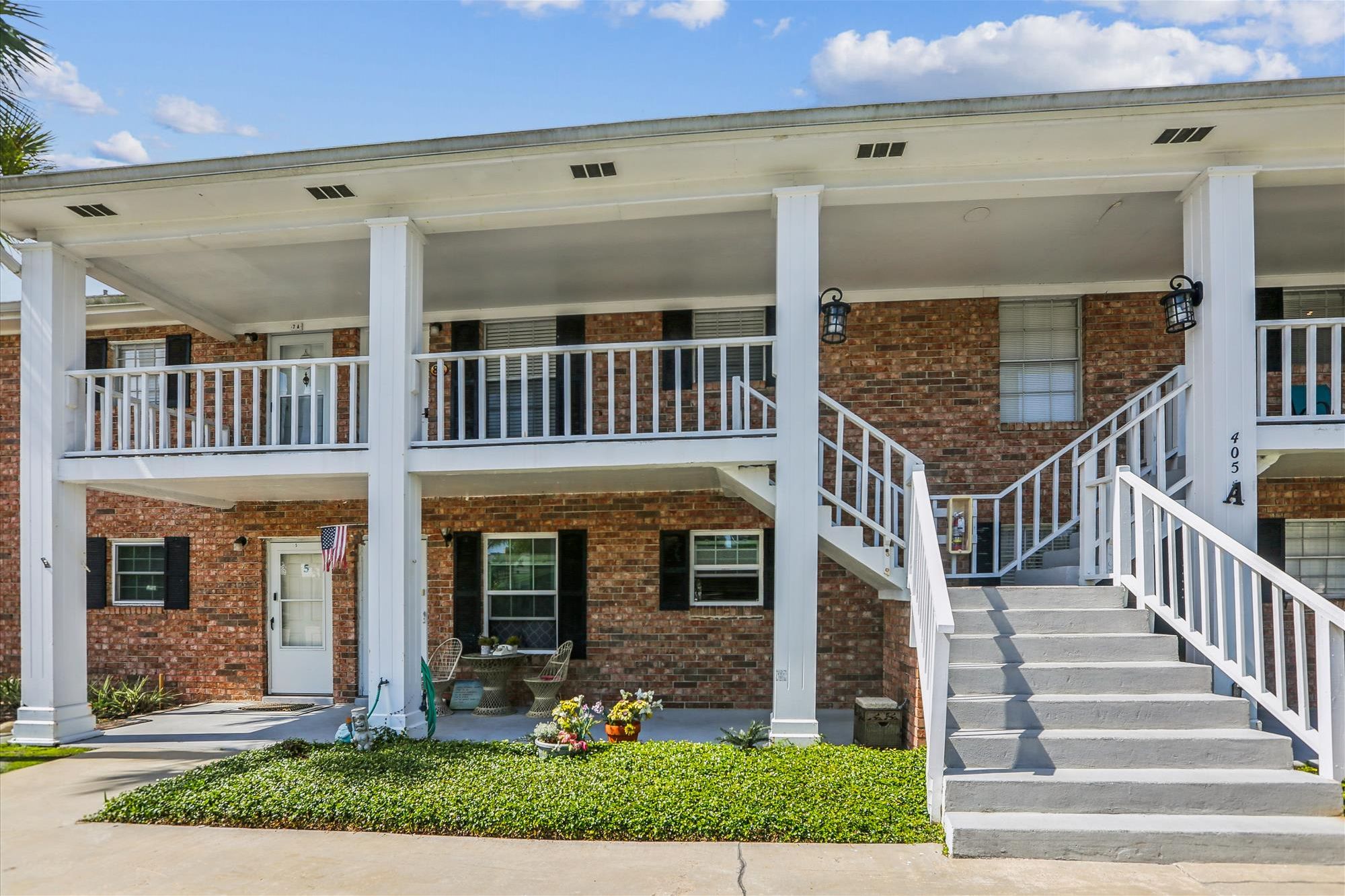 A two-story building with a covered porch, brick facade, and a staircase leading to the upper level.