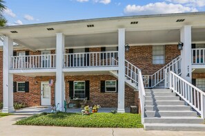 A two-story building with a covered porch, brick facade, and a staircase leading to the upper level.